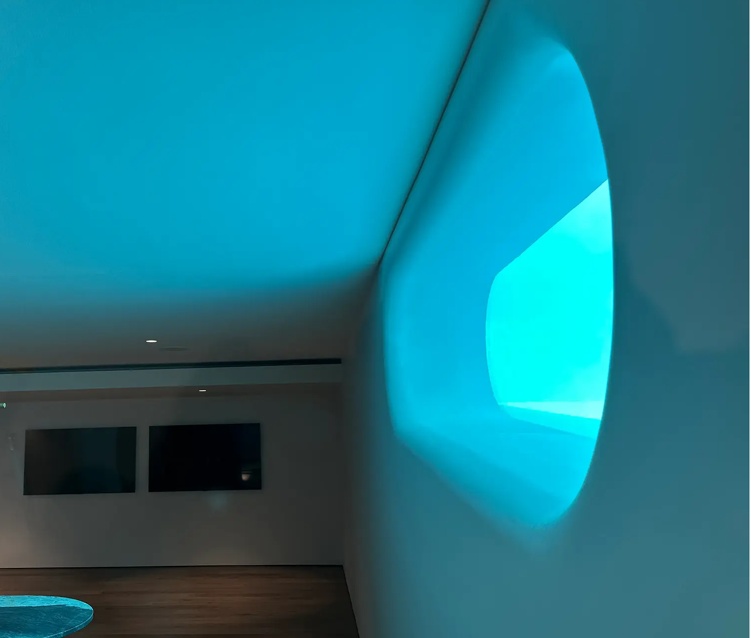 Interior view of glowing turquoise acrylic pool window casting blue light across room with wood flooring